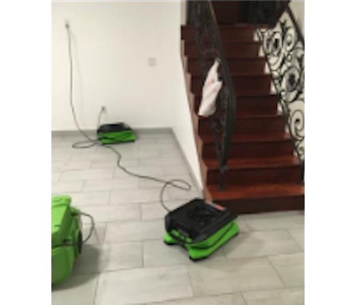 SERVPRO drying equipment on white tile floor by stairway
