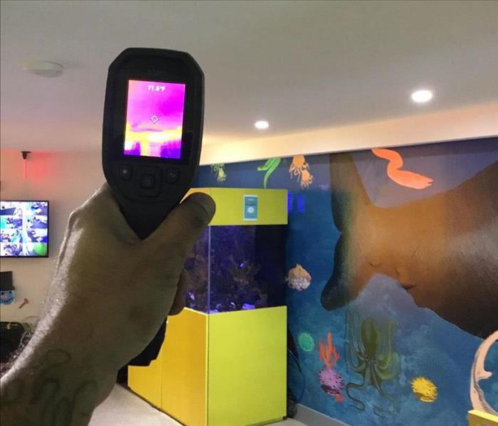 Technician operating a thermal imaging camera to detect moisture in preschool room with a fish tank