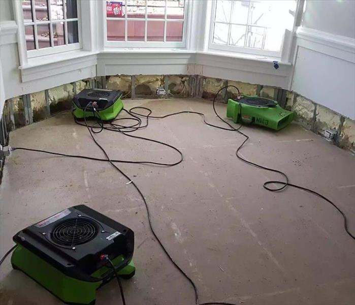 Drywall and flooring removed in a room with SERVPRO equipment on the floor. 